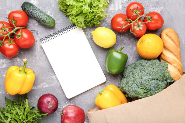 Grocery shopping bag with food and blank notepad on grey wooden  - Foto, imagen