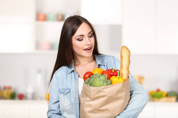 Beautiful woman holding grocery shopping bag on the kitchen - Photo, Image