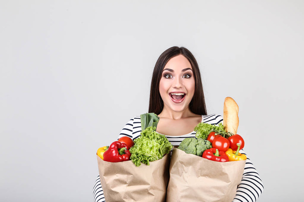 Beautiful woman holding grocery shopping bags on grey background - Foto, immagini