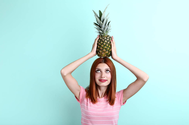 Young redhaired woman with pineapple on mint background - Foto, imagen