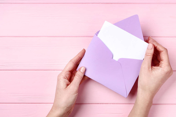 Female hands with purple paper envelope on pink wooden table - Fotoğraf, Görsel