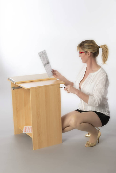 Γυναίκα κατασκευάζοντας ένα γραφείο προσωπικού υπολογιστή από ένα flatpack, χρησιμοποιώντας τις οδηγίες και ένα κατσαβίδι - Φωτογραφία, εικόνα