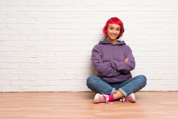 junge Frau mit rosa Haaren, die auf dem Boden sitzt und die Arme frontal verschränkt hält - Foto, Bild