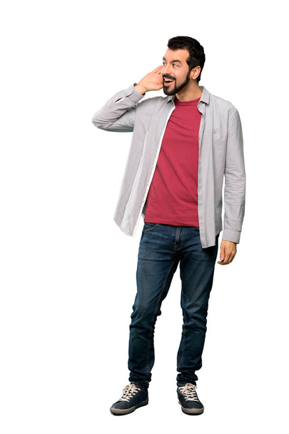 Full-length shot of Handsome man with beard listening to something by putting hand on the ear over isolated white background - Foto, Imagem