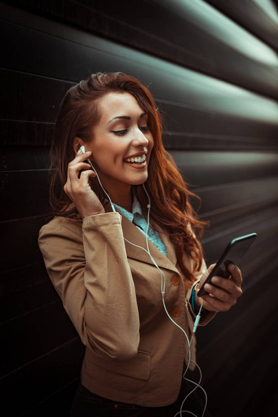 young smiling woman listening to music on smartphone in office district - Foto, Imagem