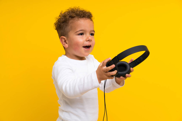 Happy kid over isolated yellow background listening music - Photo, Image