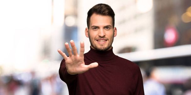 Άνθρωπος με ζιβάγκο πουλόβερ μετρώντας πέντε με τα δάχτυλά της πόλης - Φωτογραφία, εικόνα