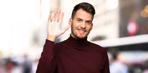 Férfi garbó pulóver tisztelegve kézzel boldog kifejezés a városban - Fotó, kép