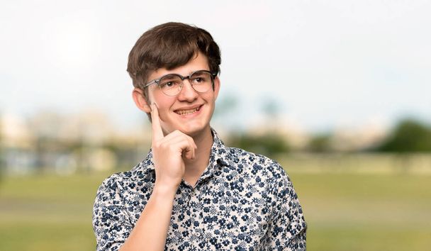 Adolescente homem com camisa de flor e óculos pensando em uma ideia enquanto olha para o ar livre
 - Foto, Imagem