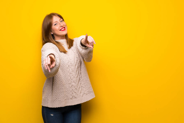 Pelirroja mujer sobre amarillo pared señala dedo en usted mientras sonríe
 - Foto, Imagen