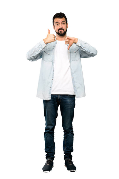 Full-length shot of Handsome man with beard making good-bad sign. Undecided between yes or not over isolated white background - Photo, Image