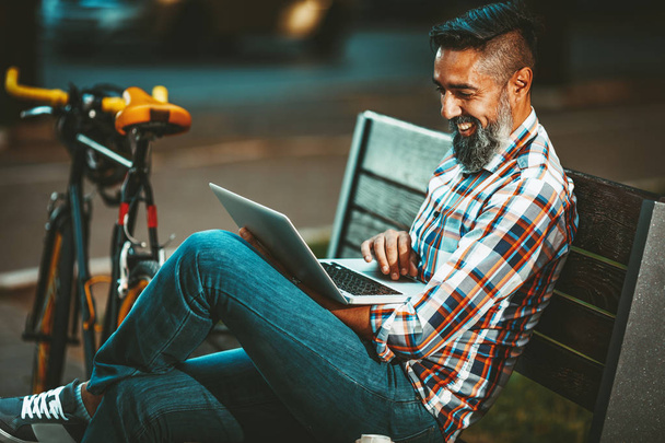 Sorrindo homem sentado no banco e trabalhando no laptop
 - Foto, Imagem