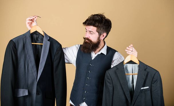 Following elegant mens style. Bearded man holding mens jackets at department store. Hipster choosing suit jacket in mens boutique. Businessman making formal mens clothing choice in closet - Fotografie, Obrázek