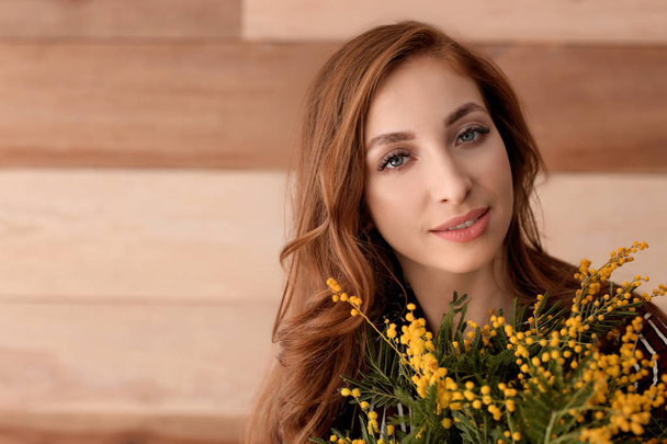 Beautiful young woman with bouquet of mimosa flowers on wooden background - Photo, Image