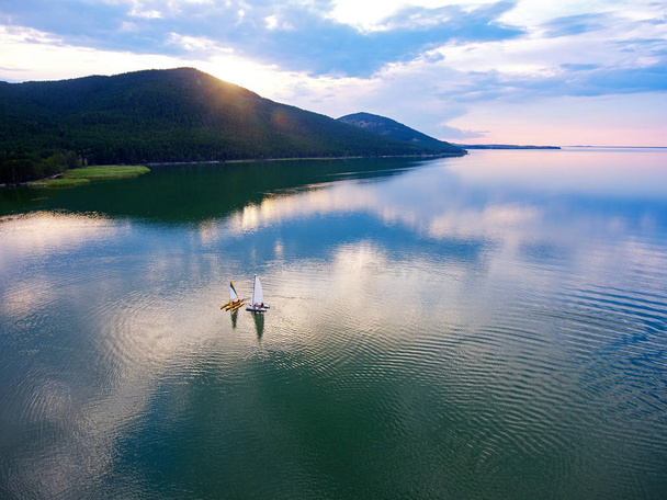 Catamaranes navegando por el lago Imantau al atardecer. Vista desde arriba. Pintoresca puesta de sol. Nubes reflejadas en el agua. Lago Imantau, Kazajstán
. - Foto, Imagen