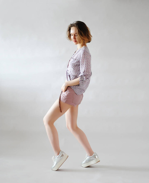 Menina elegante em shorts no fundo de luz. Roupa na moda em tons rosa. Sapatilhas na plataforma
. - Foto, Imagem
