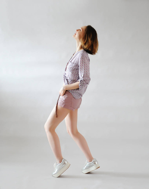 stylisches junges Mädchen in kurzen Hosen auf hellem Hintergrund. trendiges Outfit in rosa Tönen. Turnschuhe auf dem Bahnsteig. - Foto, Bild