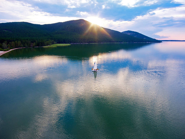 Katamaran łodzi pływających po jeziorze Imantau o zachodzie słońca. Widok z góry. Malowniczy zachód słońca. Chmury odbite w wodzie. Jezioro Imantau, Kazachstan. - Zdjęcie, obraz