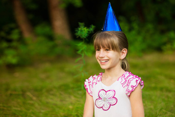 Щаслива маленька дівчинка мила і красива в святкових конусних шапочках, сидіти на траві, отримувати задоволення
 - Фото, зображення