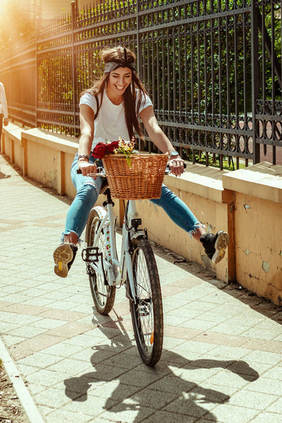 Jonge vrouw paardrijden fietsen langs stad straat in zonnige zomerdag - Foto, afbeelding