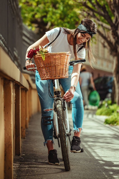 Молода жінка їде на велосипеді вздовж міської вулиці в літній сонячний день
 - Фото, зображення