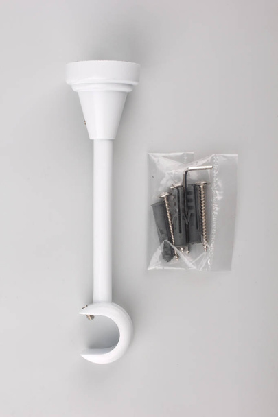White bracket for curtain rod with plastic pack of screws on grey background - Foto, Imagen