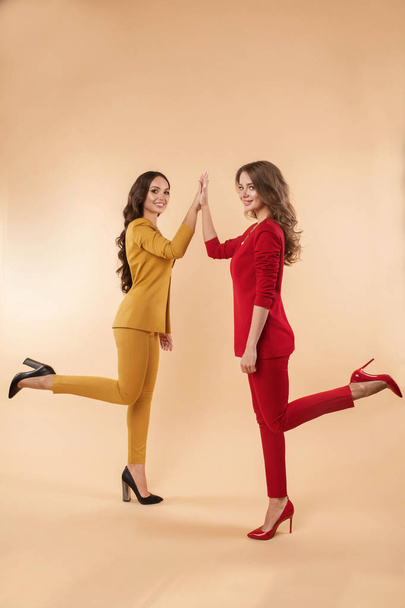 Two gorgeous colleagues in bright suits and heels giving high five. - Zdjęcie, obraz