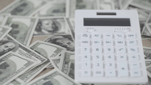 az elszórt dollár bankjegyek és a számológép szelektív fókusza a fa asztalra  - Felvétel, videó