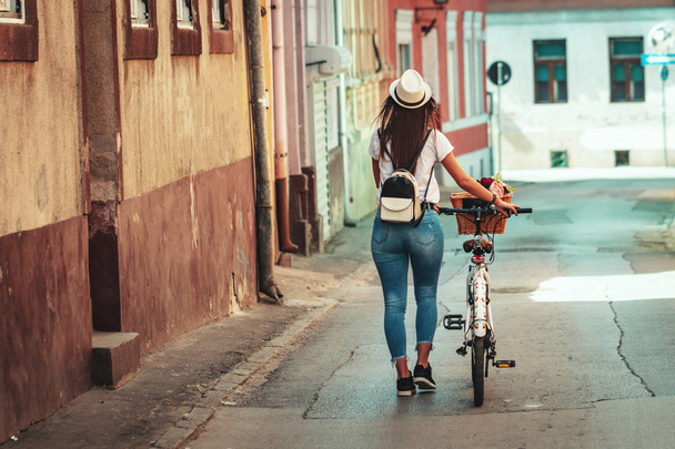 Young woman riding bike along city street in summer sunny day - Fotó, kép