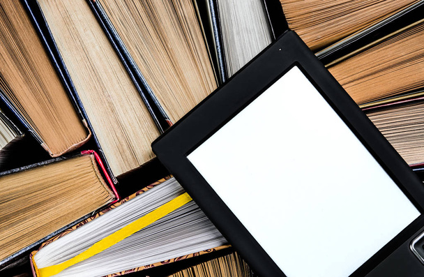 Электронная книга с белым экраном лежит на открытых разноцветных книгах, которые лежат на темном фоне, крупным планом
 - Фото, изображение