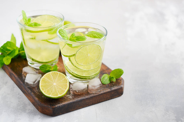 Cold refreshing summer drink with lime and mint in a glass on a gray concrete or stone background. - Foto, Imagem