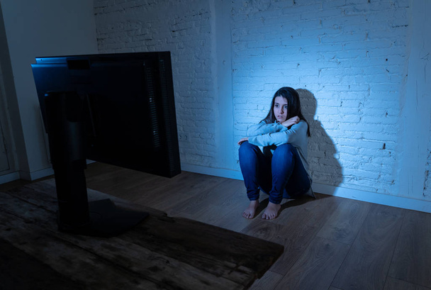 Dramatic portrait of sad scared young woman on the ground staring a computer suffering cyberbullying and harassment. Being online abused by stalker feeling desperate. Dangers of internet concept. - Photo, Image