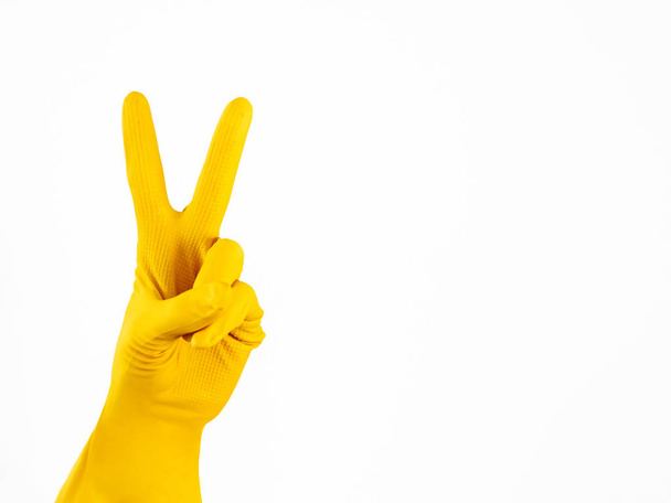 Hand in yellow rubber glove shows V on white background. Isolated Victory gesture. Symbol of good cleaning service. - Foto, immagini