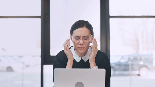 donna d'affari sconvolta in occhiali guardando il computer portatile e toccando occhiali in ufficio moderno
  - Filmati, video