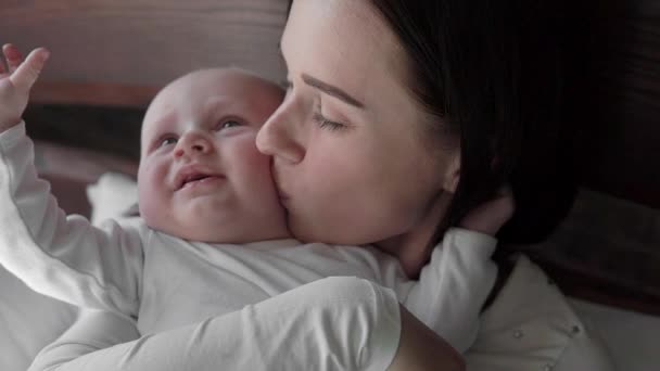 Close-up portrait of a beautiful mother smiling with baby in bed. - Imágenes, Vídeo