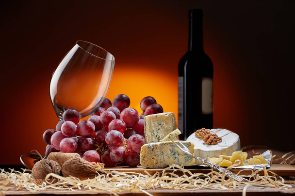 Still-life with cheese, grapes and glass and bottle of red wine. - Zdjęcie, obraz