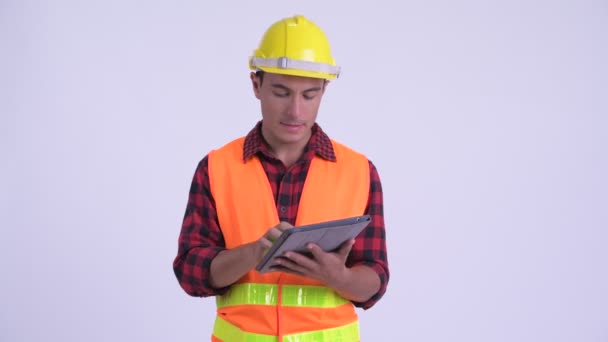 Young happy Hispanic man construction worker talking while using digital tablet - Felvétel, videó