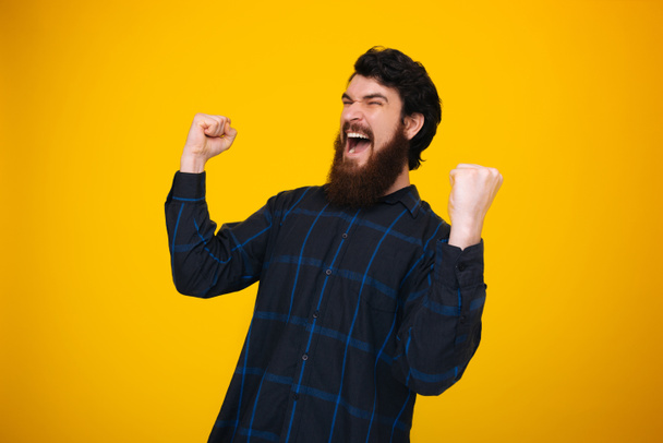 Bearded hipster making a winner gesture and screaming. Win conce - Foto, Bild