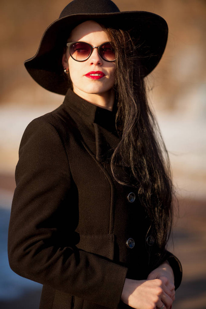Young woman posing in black coat and black hat. - Фото, зображення