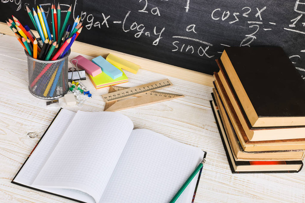 School desk in classroom, with books on background of chalk board with written formulas. Soncept Teacher's Day. - Fotoğraf, Görsel
