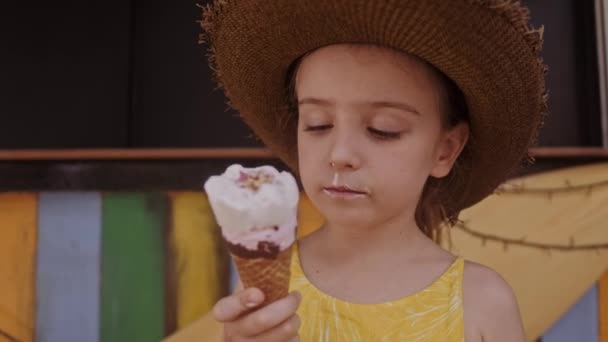 Dziewczynka w słomkowym kapeluszu jedzenia lodów na zewnątrz Street. Portret lato - Materiał filmowy, wideo