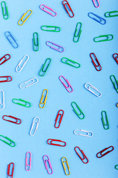 Multicolored paper clips on a blue background, pattern, copy space. - Фото, зображення