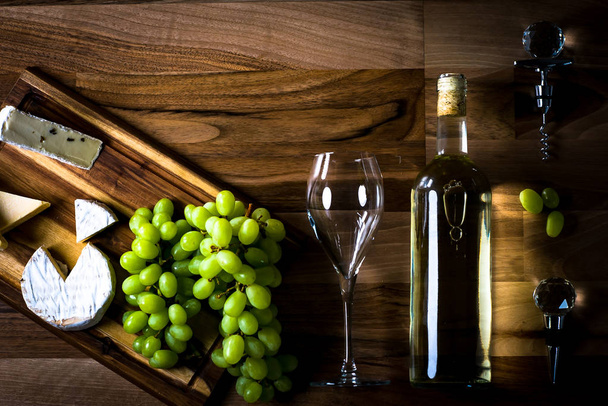 木製の背景にブドウとワインと食欲をそそるチーズ - 写真・画像