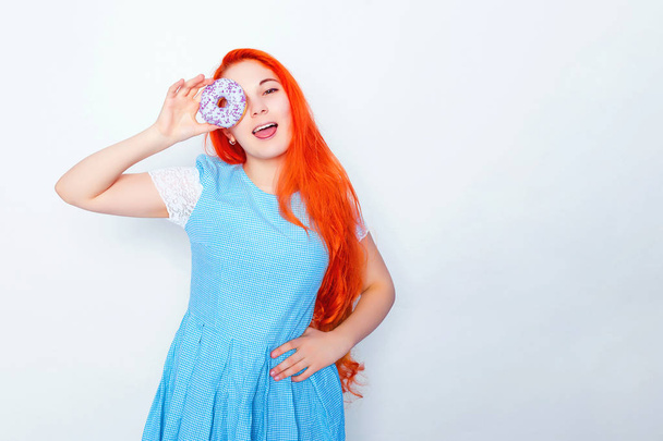 Playful teen girl in dress holding donuts on her head. Girl with long red hair on white background - Fotoğraf, Görsel