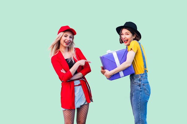 beautiful fashionable hipster best friends with big violet box present having fun on green background - Фото, изображение