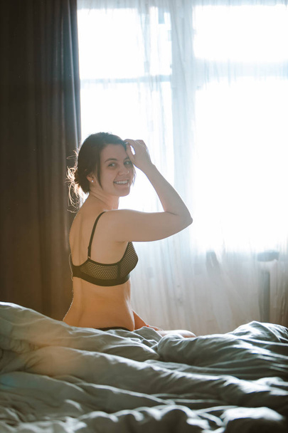 joven mujer bonita en sujetador negro sentado en la cama. hora de mañana
 - Foto, imagen