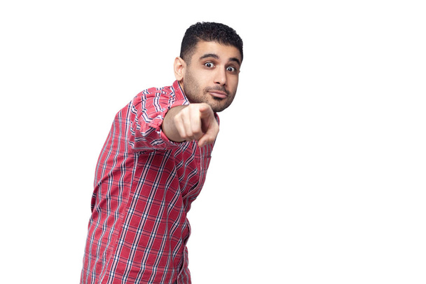 Portrait of shocked handsome bearded young businessman in red checkered shirt pointing and looking at camera with big eyes  isolated on white background. - Foto, Imagen