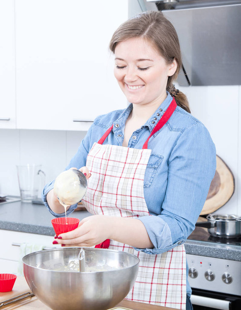 happy young woman in apron cooking delicious cupcakes in kitchen    - Foto, Imagem