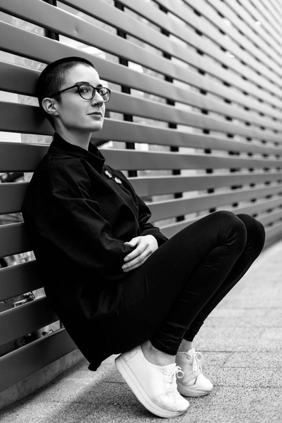 Bir duvara oturan kısa saçlı bir kadın - Fotoğraf, Görsel