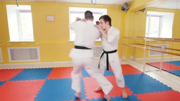 Két sportos férfi képzés az aikido képességeit a stúdióban. Egy férfi megragadja az ellenfelét, és dobja őt a padlón - Felvétel, videó
